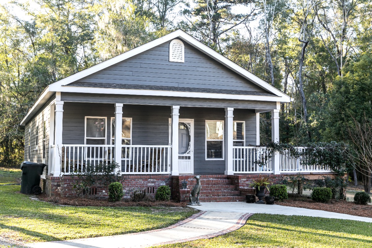 small blue gray mobile home with a front and side porch with with railing