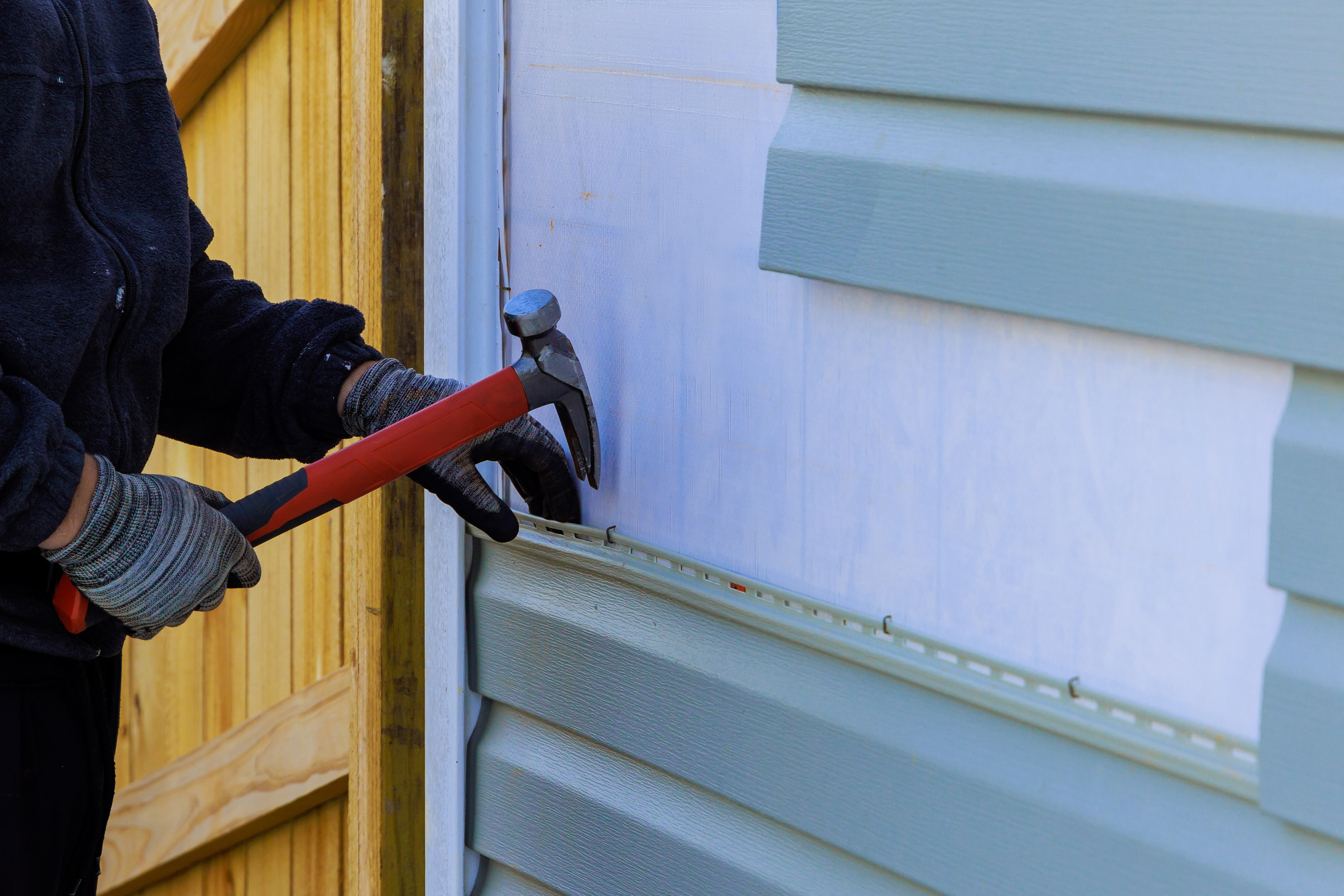 siding installer removing old siding with a hammer